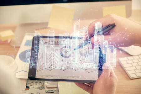 Double exposure of man's hands holding and using a digital device and city drawing.