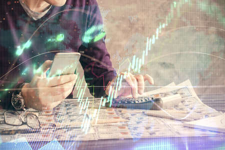 Double exposure of man's hands holding and using a digital device and forex graph drawing. Financial...