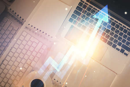 Arrows hologram drawings over computer on the desktop background. Top view. Double exposure. Concept of growth.の写真素材