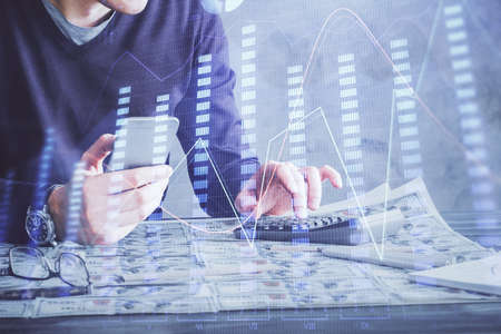 Double exposure of man's hands holding and using a digital device and forex graph drawing. Financial...