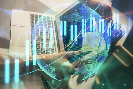 Double exposure of businesswoman hands typing on computer and financial graph hologram drawing....