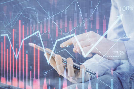 Double exposure of man's hands holding and using a digital device and forex graph drawing. Financial...