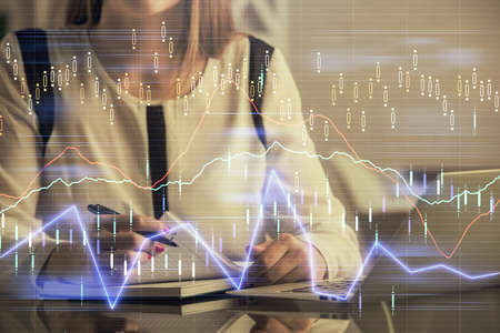 Double exposure of businesswoman hands typing on computer and financial graph hologram drawing....