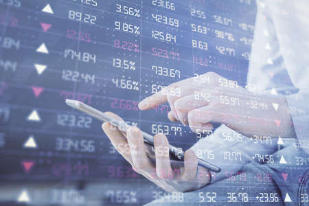 Double exposure of man's hands holding and using a digital device and forex graph drawing. Financial...