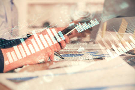 Double exposure of man's hands holding and using a phone and financial chart drawing. Market...