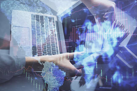 Double exposure of businesswoman hands typing on computer and financial graph hologram drawing....