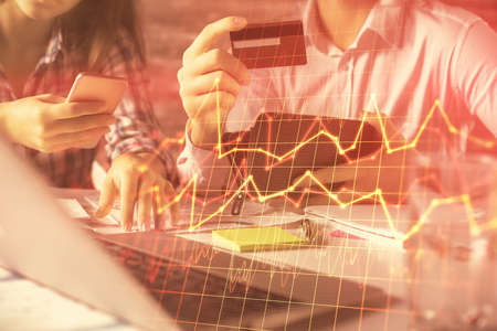 Double exposure of man and woman on-line shopping holding a credit card and forex graph hologram drawing. Stock market E-commerce pay on-line concept.の写真素材