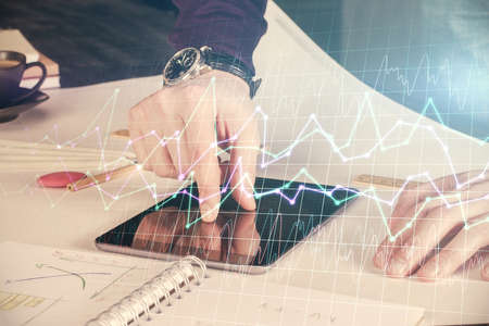 Double exposure of man's hands holding and using a digital device and forex graph drawing. Financial...