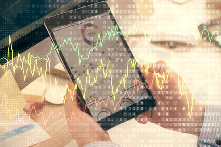 Double exposure of man's hands holding and using a phone and financial graph drawing. Analysis...