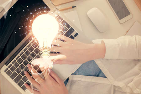 Double exposure of woman hands working on computer and light bulb hologram drawing. Top View. Idea...