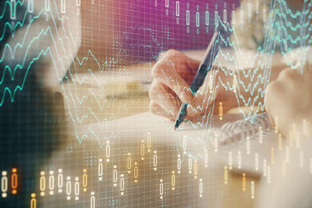 Financial forex graph displayed on hands taking notes background. Concept of research. Multi...