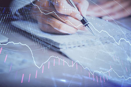 A woman hands writing information about stock market in notepad. Forex chart holograms in front....