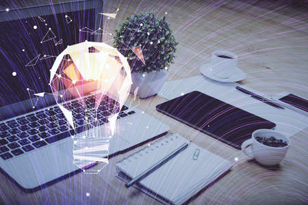 Computer on desktop in office with bulb icon hologram. Double exposure. Concept of idea.