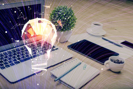 Computer on desktop in office with bulb icon hologram. Double exposure. Concept of idea.