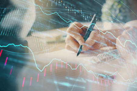 Financial forex graph displayed on hands taking notes background. Concept of research. Multi...