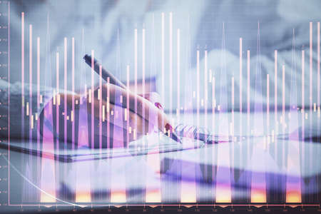 Double exposure of woman's hands making notes with forex graph hologram. Concept stock market...