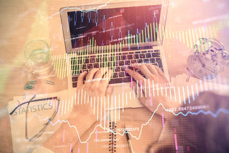 Double exposure of man's hands typing over laptop keyboard and forex chart hologram drawing. Top...