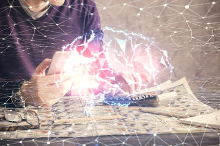 Double exposure of man's hand holding and using a digital device and brain hologram drawing. Data...