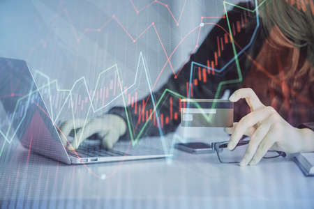 Double exposure of woman on-line shopping holding a credit card and financial graph drawing. Stock...