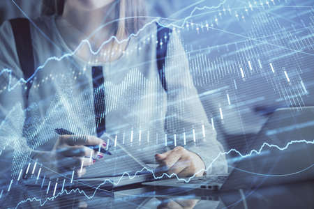 Double exposure of businesswoman hands typing on computer and financial graph hologram drawing....