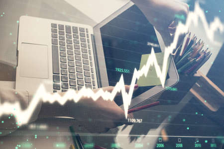 Double exposure of businesswoman hands typing on computer and financial graph hologram drawing....