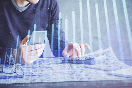 Double exposure of man's hands holding and using a digital device and forex graph drawing. Financial...