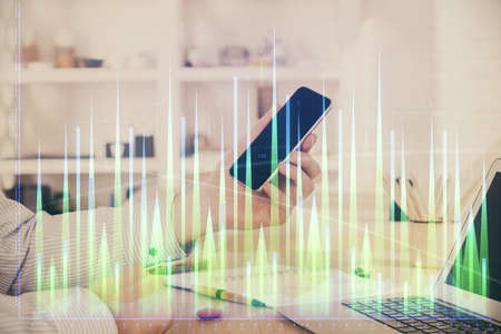 Double exposure of man's hands holding and using a digital device and forex graph drawing. Financial...