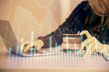 Double exposure of woman on-line shopping holding a credit card and financial graph drawing. Stock market E-commerce concept.の写真素材