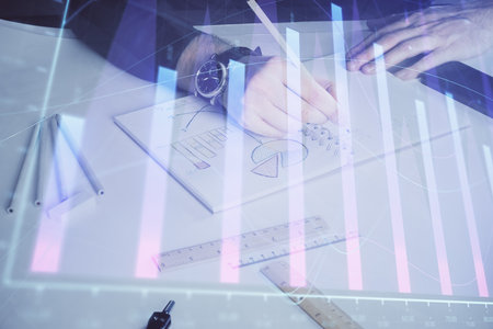 Double exposure of man's hands writing notes of stock market with forex graph background. Concept of research and trading.の写真素材