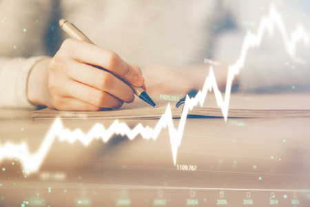 Hands writing information about stock market in notepad. Forex chart holograms in front. Concept of research. Multi exposureの写真素材