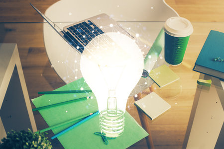 Computer on desktop in office with bulb icon hologram. Double exposure. Concept of idea.の写真素材