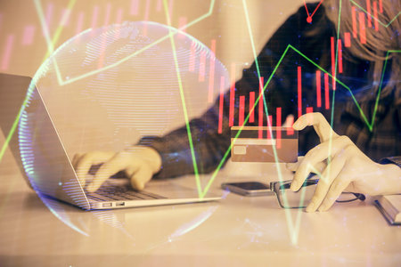 Double exposure of woman on-line shopping holding a credit card and financial graph drawing. Stock...