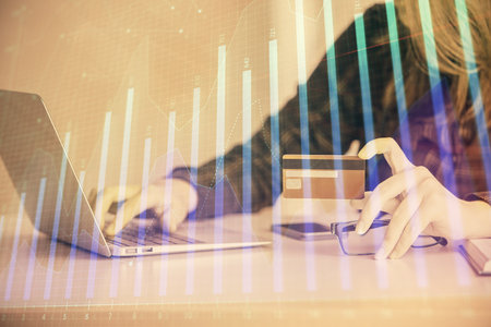 Double exposure of woman on-line shopping holding a credit card and financial graph drawing. Stock market E-commerce concept.の写真素材