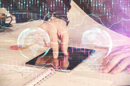 Double exposure of man's hands holding and using a digital device and forex graph drawing. Financial market concept.の写真素材