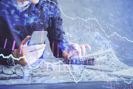 Double exposure of man's hands holding and using a digital device and forex graph drawing. Financial...