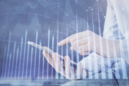 Double exposure of man's hands holding and using a digital device and forex graph drawing. Financial market concept.の写真素材