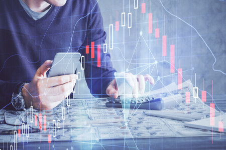 Double exposure of man's hands holding and using a digital device and forex graph drawing. Financial market concept.の写真素材