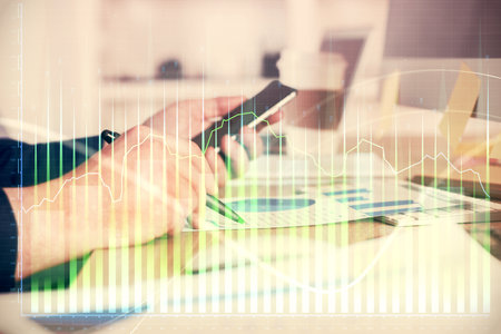 Double exposure of man's hands holding and using a phone and financial graph drawing. Analysis concept.の写真素材