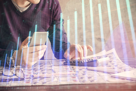 Double exposure of man's hands holding and using a digital device and forex graph drawing. Financial market concept.の写真素材