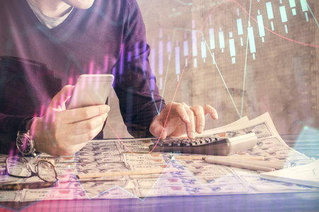 Double exposure of man's hands holding and using a digital device and forex graph drawing. Financial market concept.の写真素材