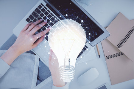 Double exposure of woman hands working on computer and light bulb hologram drawing. Top View. Idea concept.の写真素材