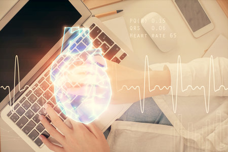 Double exposure of woman hands working on computer and heart hologram drawing. Top View. Medical Science concept.の写真素材