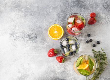 Set of summer healthy cocktails, various citrus infused waters, lemonades or mojitos, with lime and blueberries, orange and strawberries and basil, diet detox beverages, in different glasses. Copy space. Top viewの写真素材