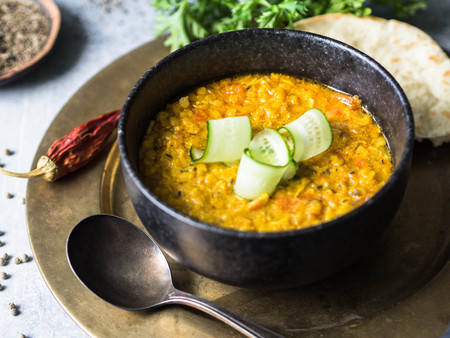Traditional Indian lentil dal soup. Hot and spicy lentil soup with fresh cucumber slices in a black stone bowl and pitaの写真素材