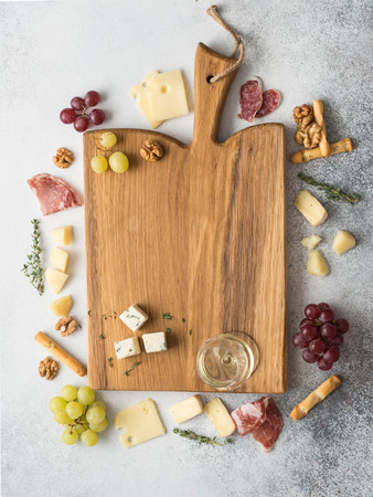 Cheese and meat wine snack set frame around the board. Variety of cheese, salami, prosciutto, bread sticks, grapes, thyme, walnutの写真素材