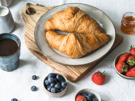 Different ingredients for breakfast. Croissants on the plate on the wood board, berries, coffee, milk and honey on a white tablecloth. Traditional French breakfast.の写真素材