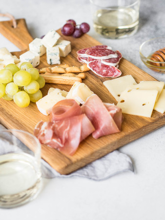 Cheese and meat wine snack set on wood board . Variety of cheese, salami, prosciutto, bread sticks, honey, grapes and two glasses with wine.の写真素材