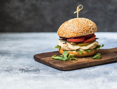 Homemade burger with grilled chicken, arugula, cheese and vegetables on a board on a gray background. Copy spaceの写真素材