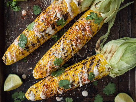 Grilled corn cobs with sauce, coriander, lime, paprika and cheese. Mexican food. Top viewの写真素材