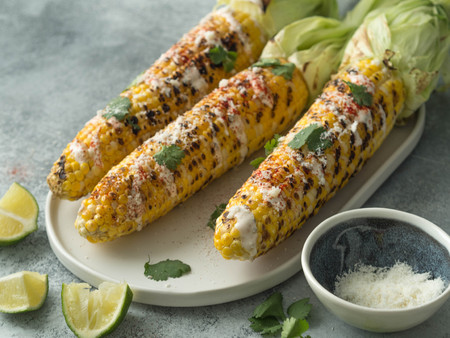 Grilled corn cobs with sauce, coriander, lime, paprika and cheese on a ceramic oval plate. Mexican food.の写真素材